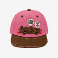 A pink and brown distressed baseball cap featuring 'Lovestones' embroidered on the front, two circular 'Spread Love' and 'Love x Trust' patches, and frayed details on the brim.